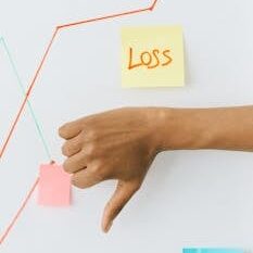 Hand showing thumbs down in front of graph indicating financial loss concept.